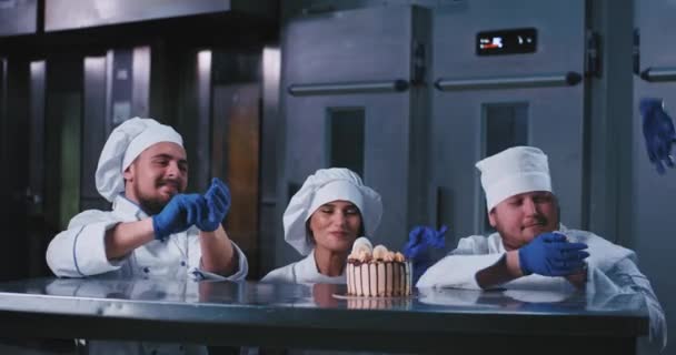 Una señora elegante con un uniforme de cocina se quita los guantes y dos panaderos a su lado hacen lo mismo, todos eligen el delicioso pastel . — Vídeos de Stock