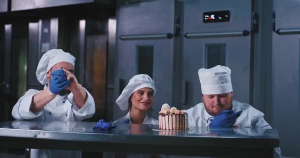 Een gracieuze dame en twee bakkers mannen die kokskleding dragen, zijn enthousiast wanneer ze beginnen met plukken bij deze verrukkelijk verjaardagscake — Stockvideo