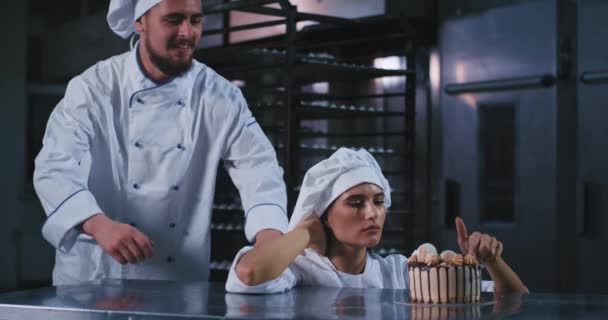 Una joven muy atractiva con un ambiente alegre disfruta de este pastel decorado, mientras que un hombre atractivo gordita se une a ella y ambos están emocionados ya que sabe muy bien. mociones lentas — Vídeos de Stock