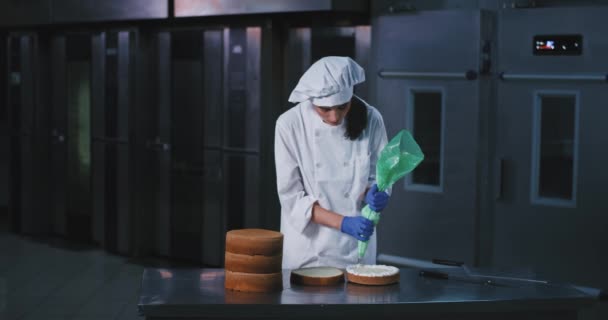 Una joven encantadora delgada con el pelo largo negro decora elegantemente el centro interior de la torta con hielo procedente de una bolsa de tuberías azul — Vídeo de stock