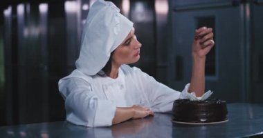 Çekici, karizmatik ve iyi giyimli genç fırıncı kadın çok güzel dekore pasta üzerinde büyüleyici kiraz tutar