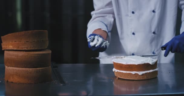 このパン屋の男は、この大きなへらを保持し、スムーズにヘラとケーキの上にクリームを広げ続けるために彼のきれいな手を使用しています, このケーキは、秘密の魅惑的に見ています — ストック動画