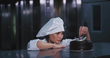 Tam bir şef kıyafetleri giymiş genç güzel bayan ağzına kiraz yakalamak kırmızı göz yerleştirilir ve gizemli o sonra sevinçle kameraya gülümsedi etrafına baktı. kırmızı epik vurdu