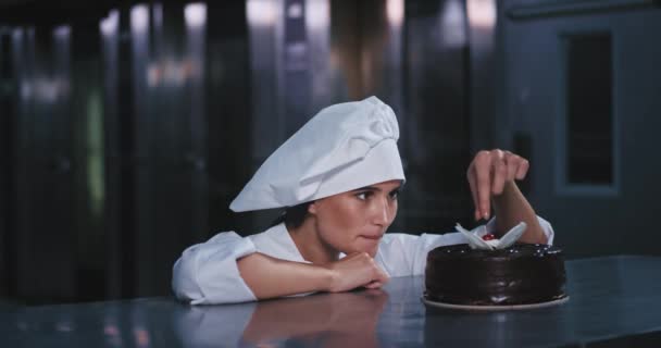 A jovem senhora padeiro magro e deslumbrante tirou a cereja do bolo de chocolate e colocá-lo em sua boca alegremente rindo de seu ato — Vídeo de Stock