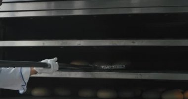 Bir çene ve şık üniforma ile fırıncı fırından pişmiş ekmek çıkarmak ve raflarda boşaltılmış