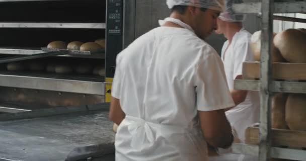 Bageriindustrin baka bröd tar bort från ugnen på Baker chef hans hjälp ordna brödet på de särskilda hyllorna. långsamma rörelser — Stockvideo