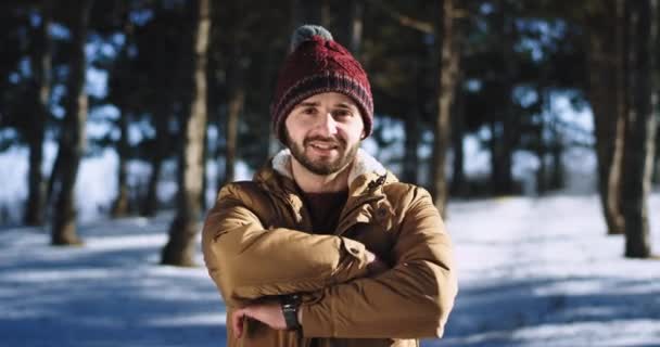 Uomo molto attraente con un grande sorriso guardando dritto alla fotocamera e sentendosi eccitato si trova in mezzo alla foresta innevata — Video Stock