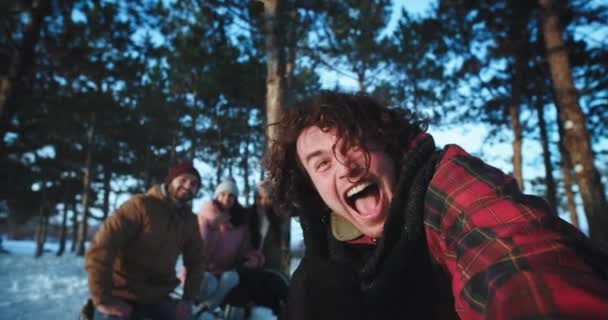 Człowiek bardzo charyzmatyczny z dużym uśmiechem i kręcone włosy z przyjaciółmi zrobić bardzo podekscytowany wideo trzymając aparat i zrobić zabawne twarze bardzo entuzjastycznie na wycieczkę zimą — Wideo stockowe