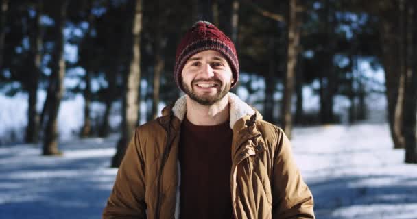 Bel ragazzo sorridente molto bello davanti alla telecamera indossa un cappello in mezzo alla foresta innevata — Video Stock