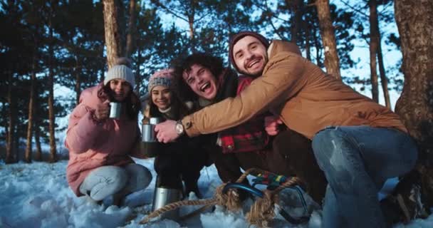 カメラの前で多民族の友人の大きなグループは、アイアンカップからいくつかの熱いお茶を飲んで、時間を楽しんで森の中で冬の日の時間を楽しみます — ストック動画