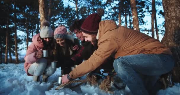 Большая группа харизматичных друзей турист в середине зимы в лесу они пьют горячий чай из железной чашки и отдохнуть после тяжелого дня поездки — стоковое видео