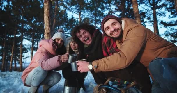 Multiethnisch charismatische Gruppe von Freunden, die in einem Winter mitten im Wald unterwegs sind, machen Pause und trinken ein paar heiße Getränke aus Eisentasse — Stockvideo