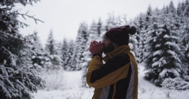 Νεαρός τουρίστας ταξιδεύει μόνος του σε μια δύσκολη χειμωνιάτικη μέρα σταμάτησε στη μέση του χιονισμένο δάσος και να πάρει μερικά ζεστά ροφήματα για να ζεσταθεί απολαμβάνει τη θέα γύρω του — Αρχείο Βίντεο