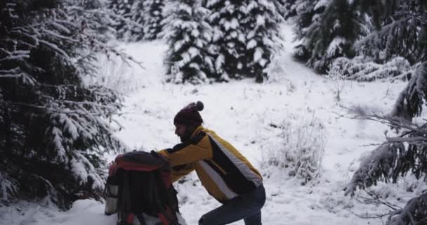Utrustad ung man turistresa genom den hårda vintern i mitten av snöiga skogen han njuter av tiden dricka lite hett te från en järnkopp — Stockvideo