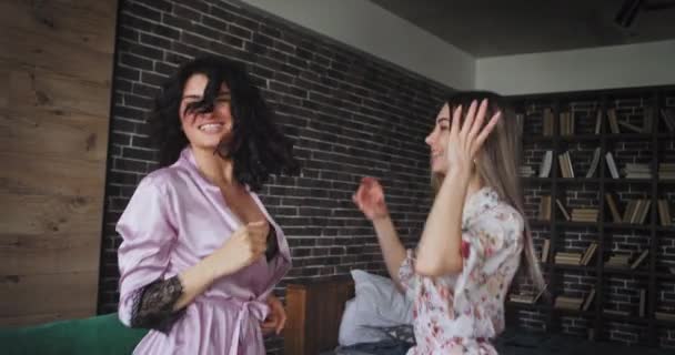Het springen van charismatische dames in pyjama in de ochtend hebben een geweldige sfeer in verbazingwekkende Studio appartement ze genieten van de tijd voor de camera — Stockvideo