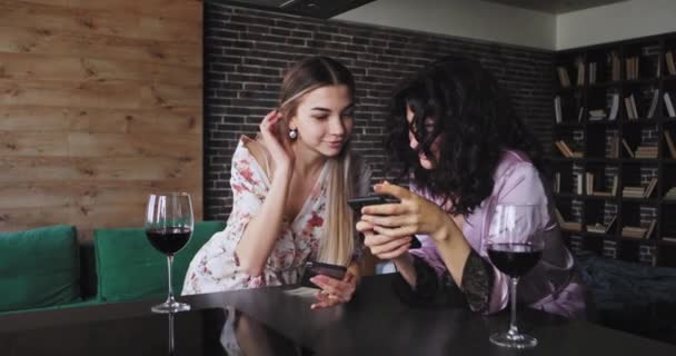 У сучасній квартирі дві жінки дуже харизматично використовують смартфон, щоб написати повідомлення під час пиття келихів вина в піжамі вони насолоджуються дружнім часом разом — стокове відео
