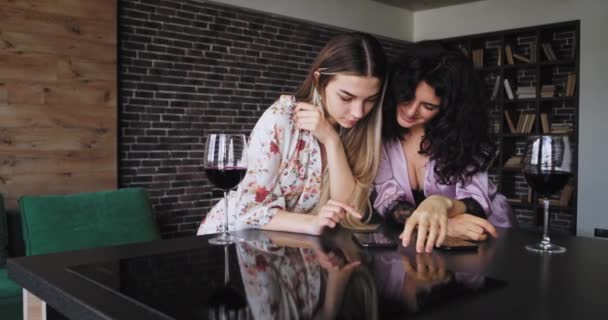 Twee mooie dames in pyjama hebben een geweldige avond samen terwijl het drinken van een glazen wijn met behulp van hun smartphone om te chatten met iemand die ze genieten van het moment samen — Stockvideo