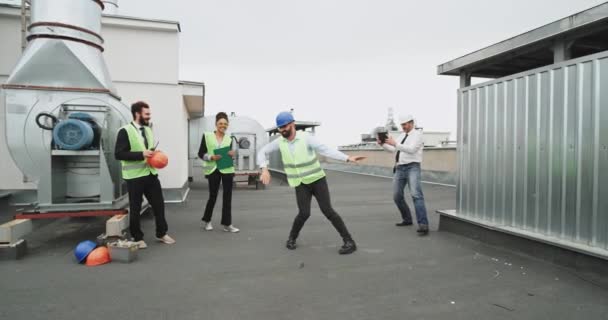 Ein Bauarbeiter zeigt seine Hip-Hop-Bewegungen, während ein Mann mit weißem Bauhut ihn auf einem iPad filmt und seine Freunde zuschauen — Stockvideo