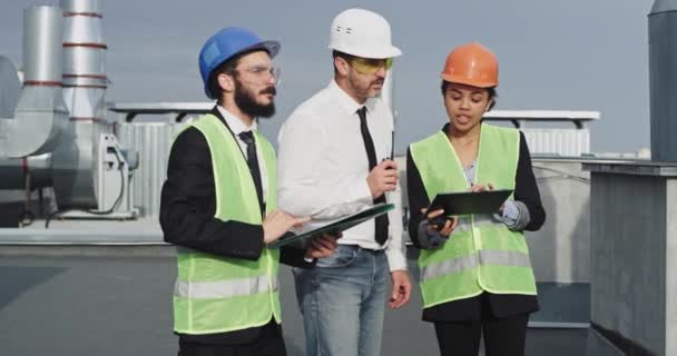 若いビジネスマンとタブレットやシートから建物の計画を分析エンジニアや建築家の建設業界グループ — ストック動画