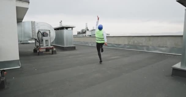 Man Ingenieur oder Architekt erledigen die Arbeit auf der Baustelle glücklich, er beginnt zu tanzen und fällt auf die Knie auf der Oberseite des Gebäudes, während er bei der Ration spricht — Stockvideo