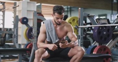 Genç, yakışıklı bir adam, o spor salonunda iken telefonuna bakar ve su içmek için devam eder