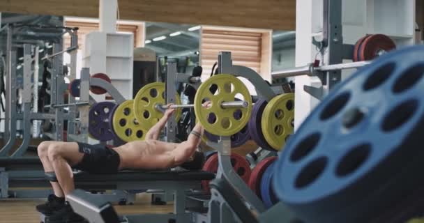 Un ragazzo molto in forma in una palestra di atleti, lavora su alcuni pesi molto pesanti, si sta comportando bene — Video Stock