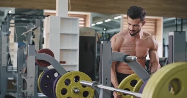 Un gran hombre musculoso guapo está poniendo más pesas en la barra, ya que está siendo saludable y haciendo ejercicio — Vídeos de Stock