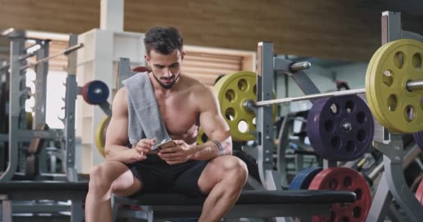 Een aantrekkelijke jongeman drinkt water tijdens het trainen, hij ziet er erg moe uit als hij probeert om een gezond leven te behouden — Stockvideo