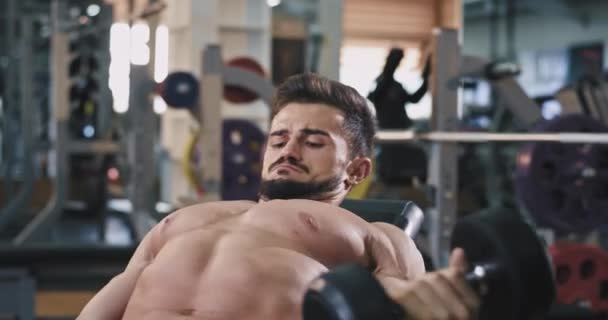 Парень из спортзала поднимает тяжести, поигрывая мышцами, и делает идеальный пресс. — стоковое видео