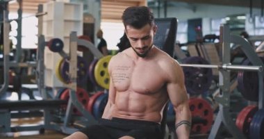 Spor salonunda spor yapan fit bir vücuda sahip genç adam, pazılarının içinde ağırlıkları kaldırıyor.