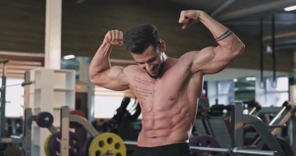 Schöner Mann in einem großen Fitnessstudio, der seine Muskeln vor der Kamera spielen lässt, glücklich lächelt er groß — Stockvideo