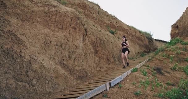 Eine junge athletische Frau rennt ein paar Stufen in den Bergen hinunter — Stockvideo