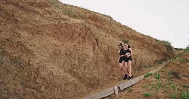 Δύο σπορ κορίτσια περπατούν μαζί με ευχαρίστηση κάτω από τα σκαλιά και πάνω στην παραλία — Αρχείο Βίντεο