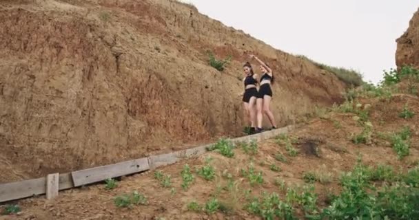 Две девушки в черной спортивной одежде и на скорости спускаются по лестнице на песок, они здоровы — стоковое видео