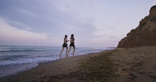 Prachtig uitzicht op het landschap op het strand twee aantrekkelijke dames die in de ochtend met de sportkleding samen rennen — Stockvideo