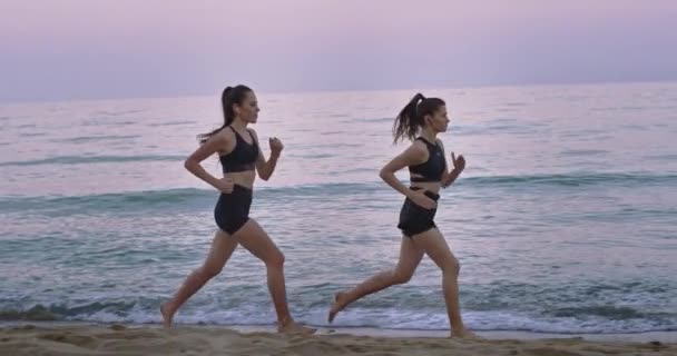 Paisaje con vista al mar dos damas corriendo por la playa por la mañana juntas disfrutando del momento — Vídeo de stock