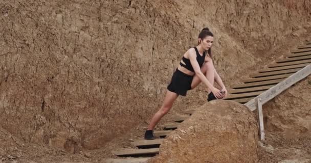 Mooi uitziende jonge vrouw oefeningen stretching poses op houten trappen met verbazingwekkende rotsen op de achtergrond — Stockvideo