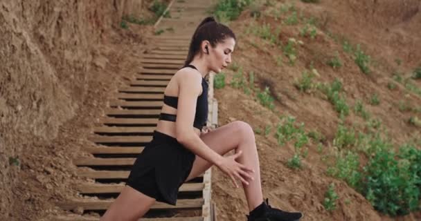 Details closeup good looking lady stretching her legs on wooden steps beside of big rocks in a good sunny day — Stock Video