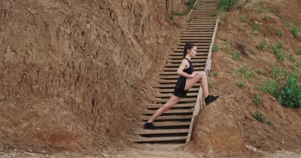 Sportliche Frauen machen morgens ein hartes Workout, strecken die Beine draußen neben den Holztreppen und hören Musik aus drahtlosen Kopfhörern. — Stockvideo