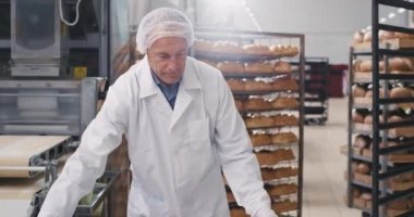 Beyaz üniformalı yaşlı fırıncı yük hamur raf fırın, büyük üretim, gıda sektöründe diğer bölüme taşınacak