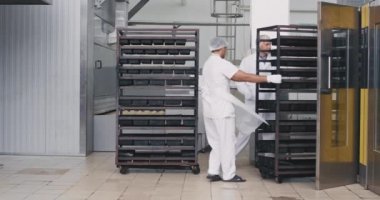 Gıda fırın mühendisi ve onun yardım yük endüstriyel fırından raflar , onlar özel ekipman beyaz üniforma giyiyor , büyük üretim karizmatik işçiler