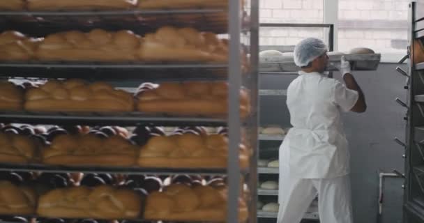 Рабочий процесс в большой пекарне производства два профессиональных рабочих загрузить сырой хлеб на печь другой работник в белой форме транспортировал свежий хлеб в другом разделе — стоковое видео