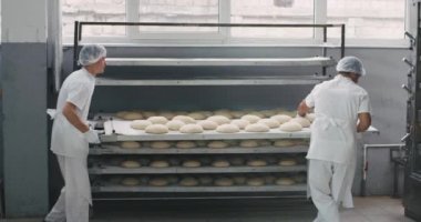 Büyük bir fırın sektöründe endüstriyel fırın makinesinde raftan Ham ekmek yükü, ana fırıncı özel bir güzel üniforma etrafında yürüdü , raflar ile diğer işçi taze taşınan