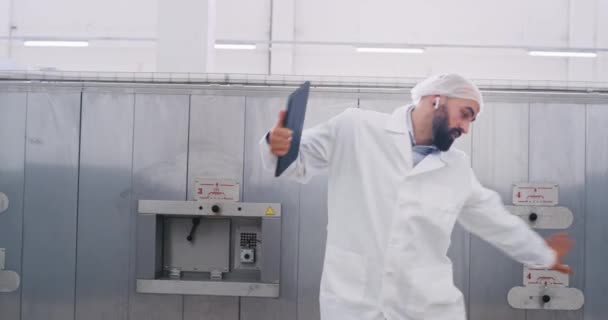 Dancing excited manufacturing worker in a special protect uniform while he walking to the industrial machine he giving five to his colleague walking beside of industrial machine open the electronic — Stock Video