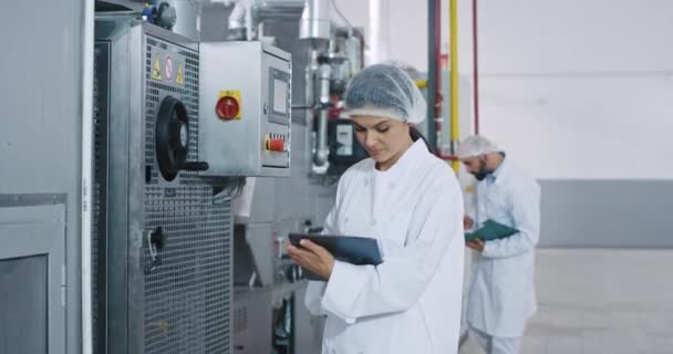Al mattino due bellissimi ingegneri dell'industria manifatturiera controllano la macchina industriale e prendono appunti sul tablet elettronico — Video Stock