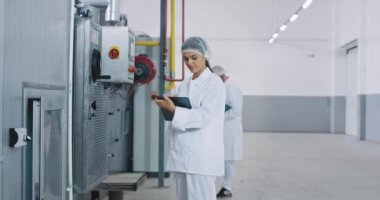 Büyük bir fırın sektöründe ticari görünümlü mühendis kadın endüstriyel makine kontrol o onun yeni nesil tablet arka plan eski fırıncı etrafında yürüyüş ve diğer mühendis bazı notlar yapmak