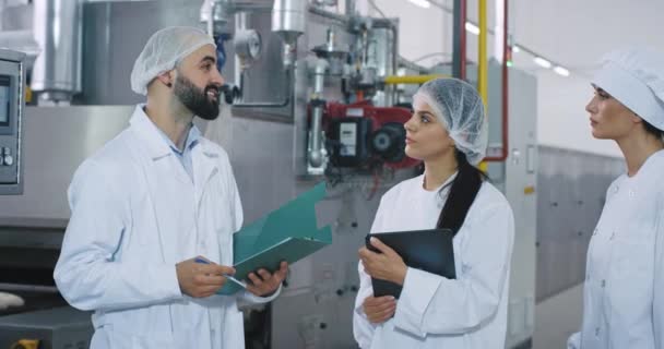 Reunión en la industria de la panadería ingeniero de fábrica con una barba que explica a los trabajadores de la panadería cómo utilizar la máquina industrial todo lo que llevan ropa especialmente blanca. tiro en épica roja — Vídeo de stock