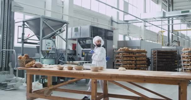 In einer Bäckereibranche Großes Video eines tanzenden Bäckers, der Musik aus drahtlosen Kopfhörern hört und mit einem Teig spielt, bevor er ein rohes Brot backt — Stockvideo