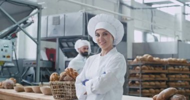 Inanılmaz bir kadın fırıncı ticari yüzü kameraya düz bakarak ve sevimli arka plan onun meslektaşı fırıncı dans ve masa çalışmaları yanında komik hareket gülümseme. yavaş hareketler