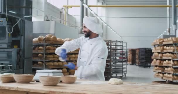 Charismatische bakker met baard in een grote bakkerij-industrie dansen tijdens het werken aan zijn tafel neem het deeg en zet op de schaal van de bakkerij. 4k — Stockvideo